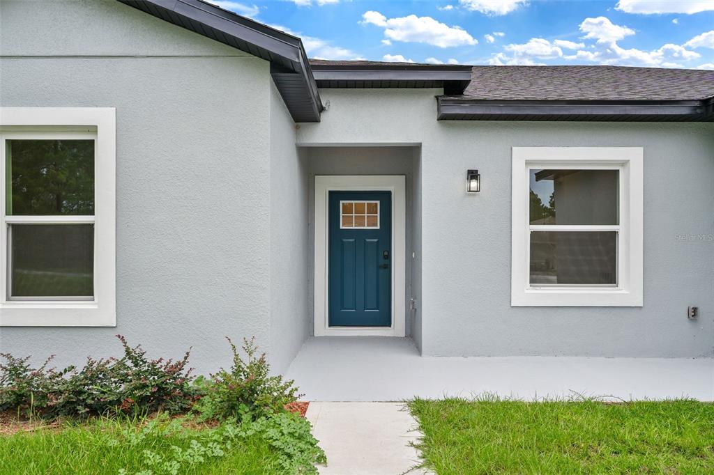 A light gray house exterior features a blue front door and two white-framed windows — 15301 SW 50TH AVENUE ROAD, OCALA, FL