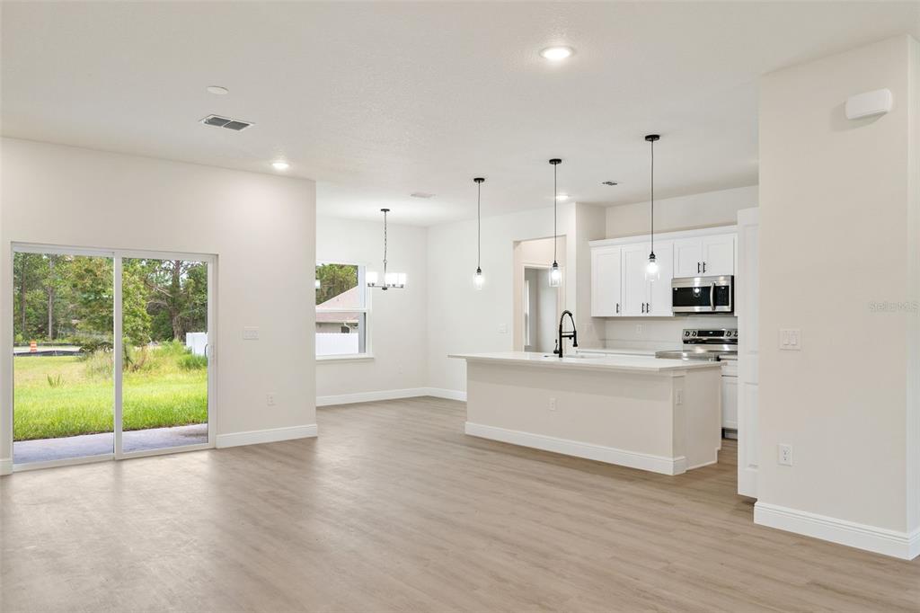 An open-concept kitchen and dining area features white cabinetry, a central island, and sliding doors — 15301 SW 50TH AVENUE ROAD, OCALA, FL