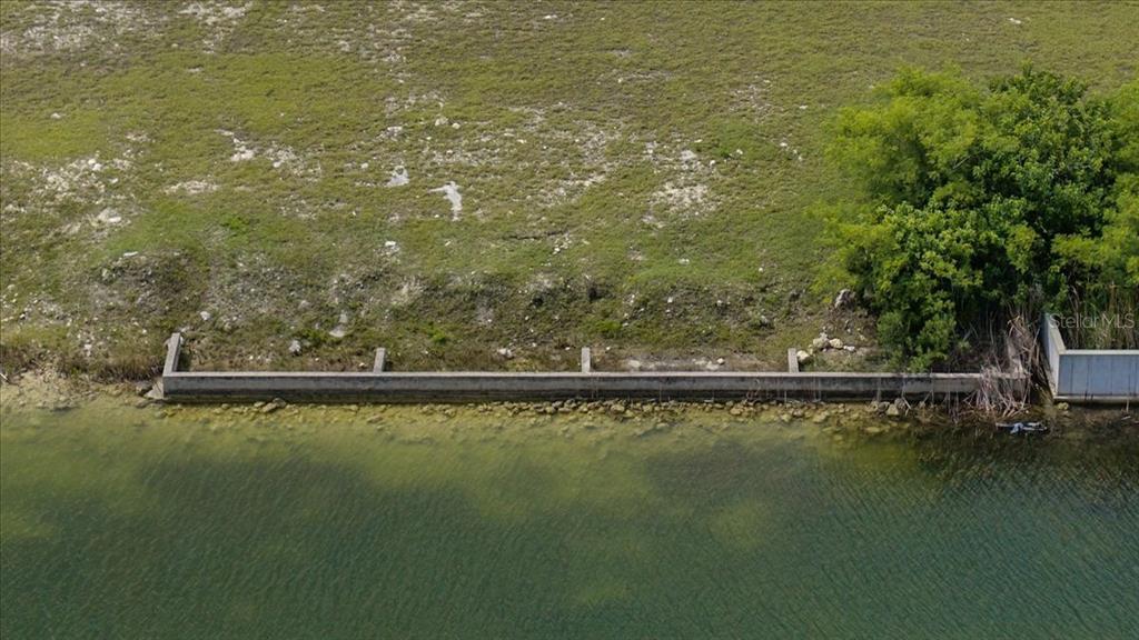 An aerial view shows a concrete seawall bordering a grassy lot next to a body of water — 3487 BLUEFISH DRIVE, HERNANDO BEACH, FL