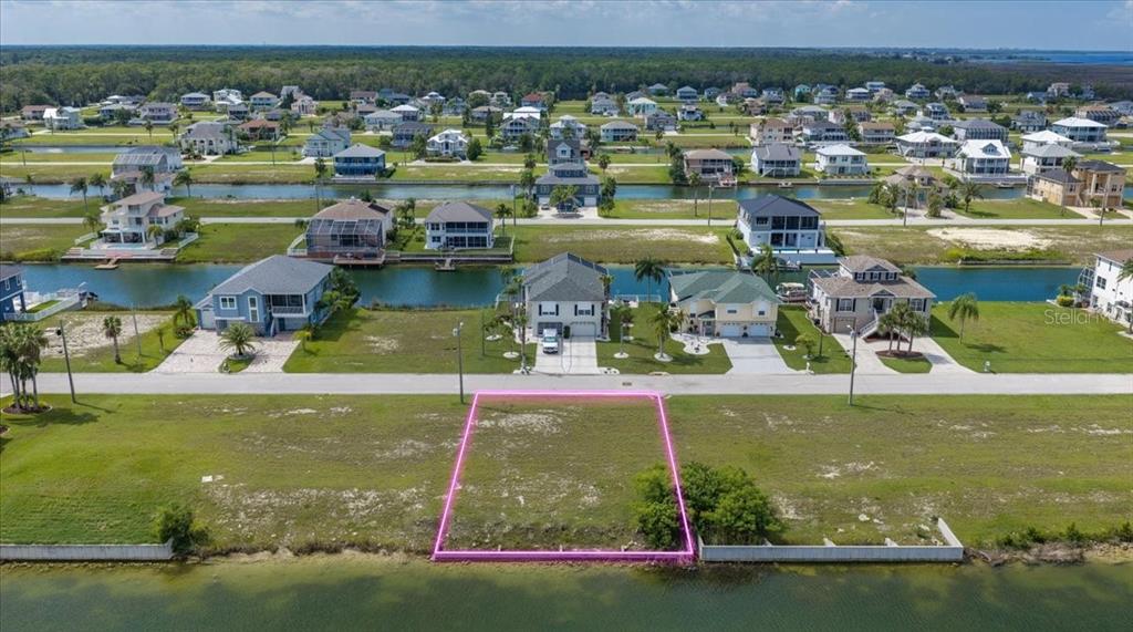 An aerial view shows a vacant waterfront lot with a seawall in front of houses — 3487 BLUEFISH DRIVE, HERNANDO BEACH, FL