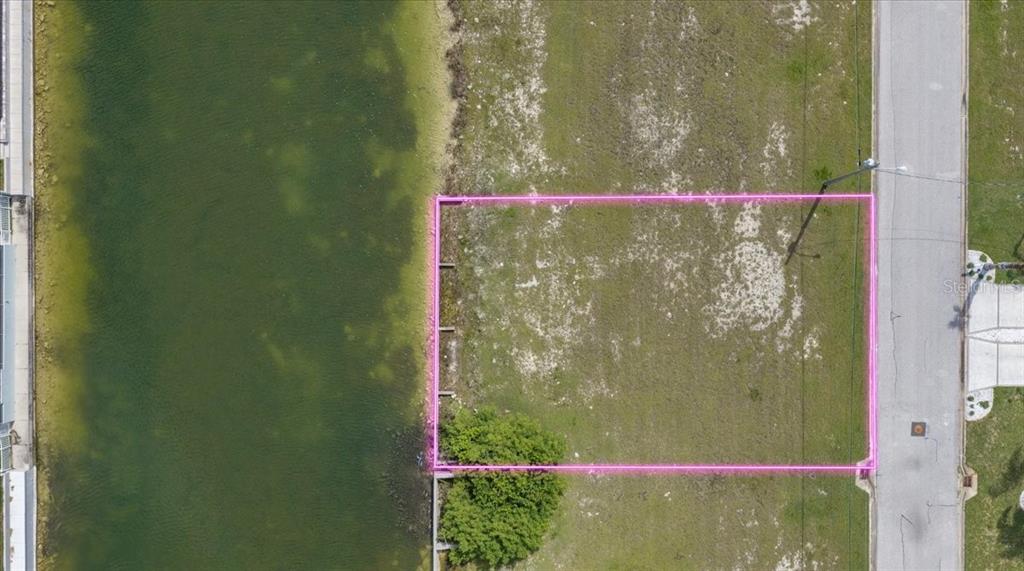 An aerial view shows a vacant waterfront lot outlined in pink across from residential houses — 3487 BLUEFISH DRIVE, HERNANDO BEACH, FL