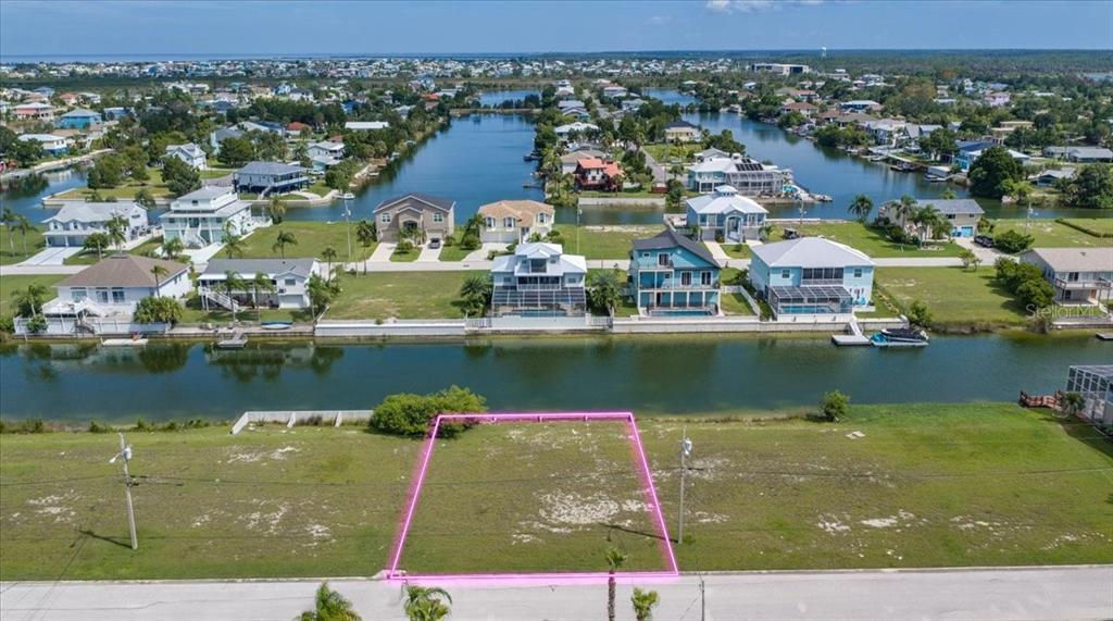 An aerial view shows a vacant, rectangular waterfront lot outlined in pink next to a road — 3487 BLUEFISH DRIVE, HERNANDO BEACH, FL