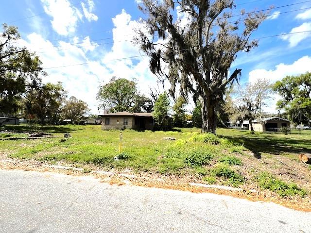 A single-story house sits on a grassy lot with large trees under a blue sky — 980 BERKLEY ROAD, AUBURNDALE, FL