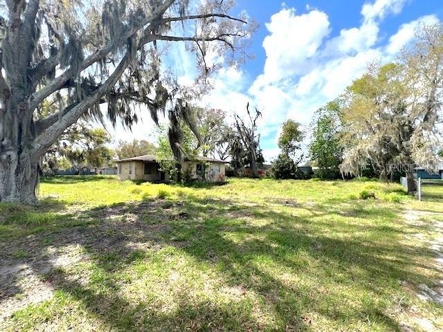 A small, weathered house sits in a grassy lot shaded by large, moss-covered oak trees — 980 BERKLEY ROAD, AUBURNDALE, FL