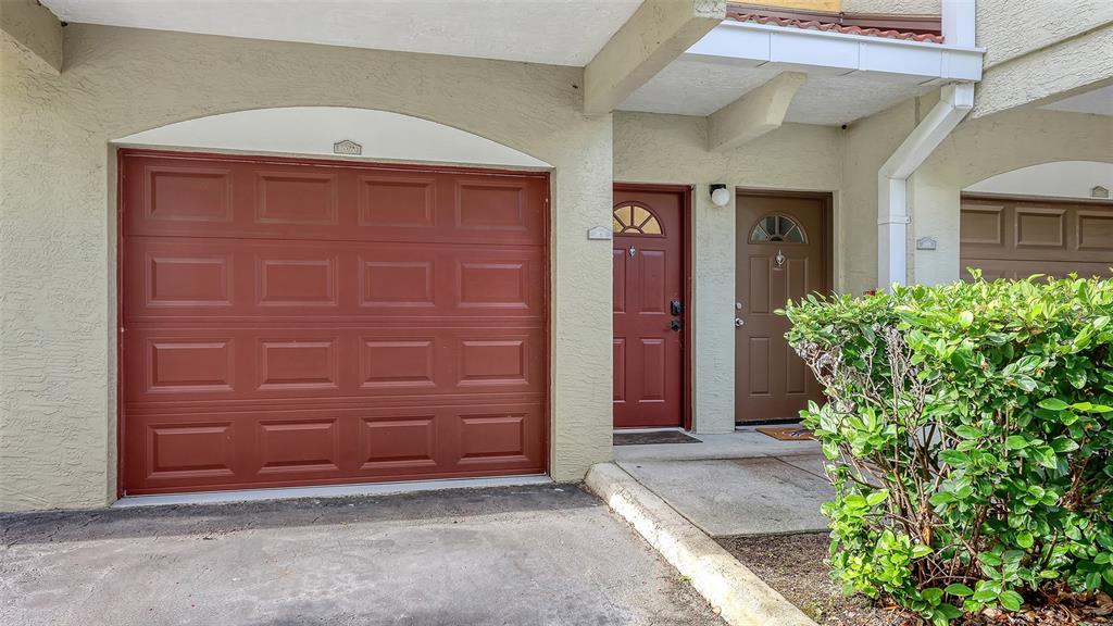 A tan stucco building exterior features a red garage door and two adjacent entry doors — 5001 BARALDI CIRCLE UNIT 22-202, SARASOTA, FL