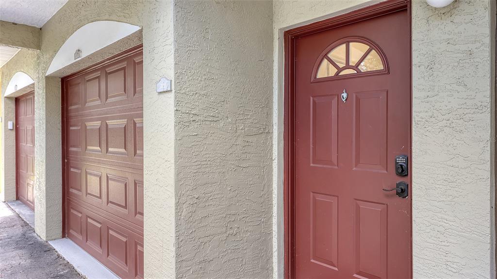 A red front door and a matching garage door are set into a textured beige wall — 5001 BARALDI CIRCLE UNIT 22-202, SARASOTA, FL