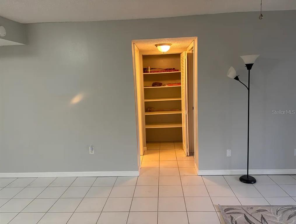 A room with light gray walls, white tile flooring, a floor lamp, and a walk-in pantry — 810 OAKGROVE DRIVE UNIT 175, BRANDON, FL
