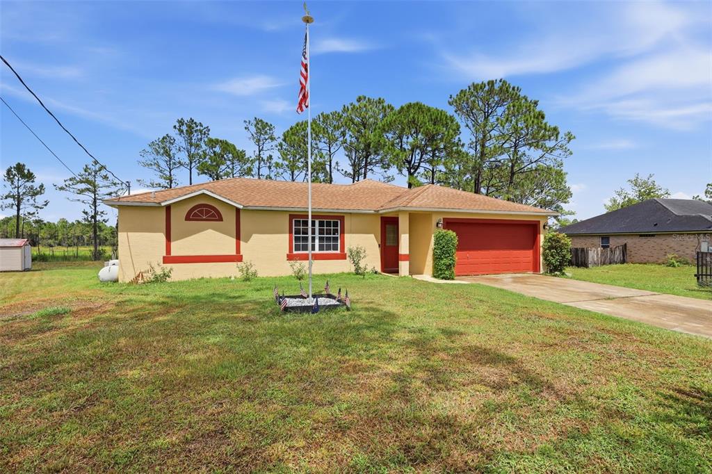A single-story house with a tan exterior, red trim, a garage, and a flagpole — 2772 PELHAM CIRCLE, DELTONA, FL