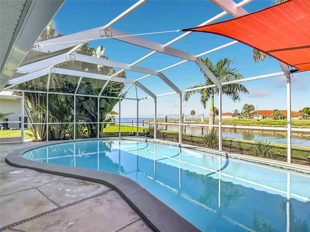 A screened-in pool patio features a dining set, a shade sail, and a waterfront view — 4449 CREWS COURT, PORT CHARLOTTE, FL