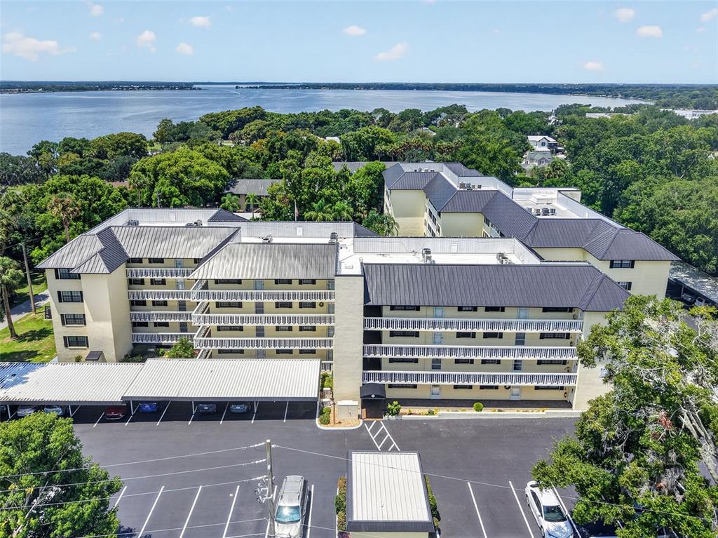 An aerial view shows a multi-story apartment building with a parking lot and waterfront background — 101 N GRANDVIEW STREET UNIT 203, MOUNT DORA, FL