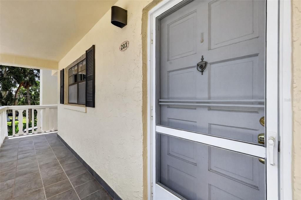 A covered balcony features a tiled floor, a white railing, and a gray screen door — 101 N GRANDVIEW STREET UNIT 203, MOUNT DORA, FL