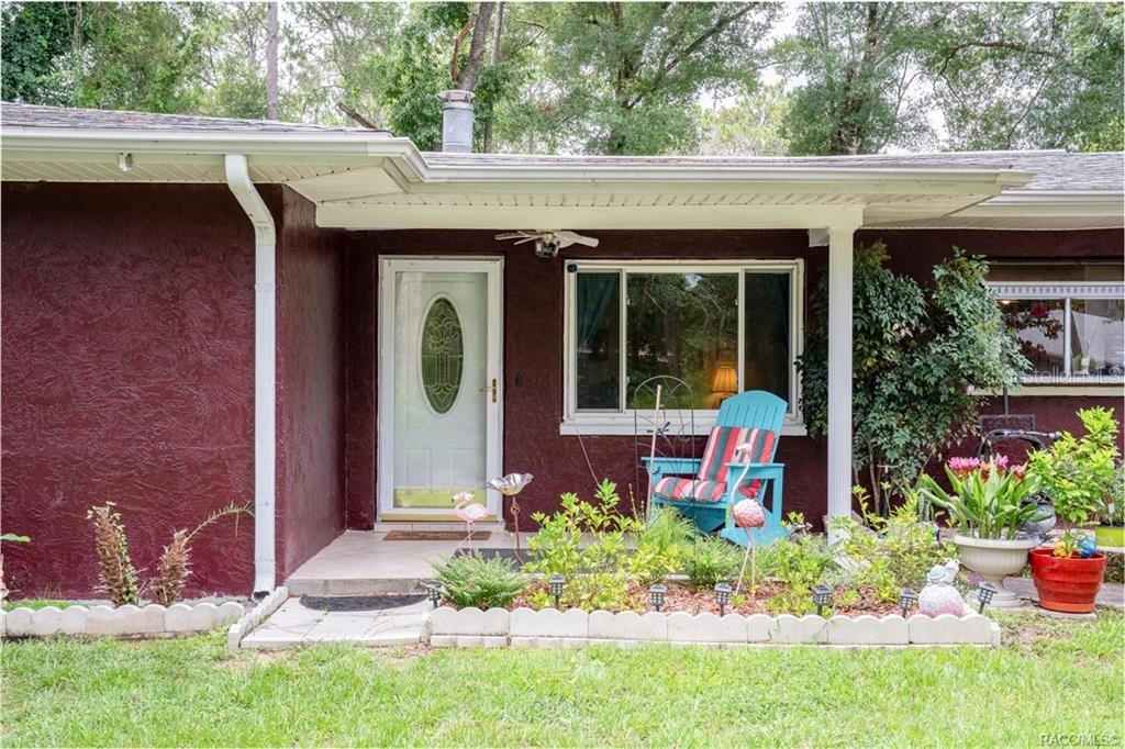 The exterior of a house features a dark red stucco wall, a white front door, and landscaping — 6046 E LORING LANE, INVERNESS, FL