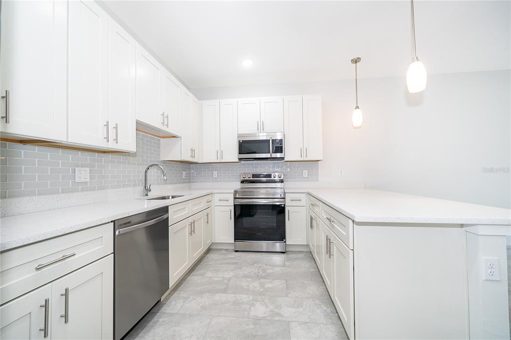 A modern kitchen features white cabinets, stainless steel appliances, a gray tile backsplash, and countertops — 1657 CUMIN DRIVE, KISSIMMEE, FL