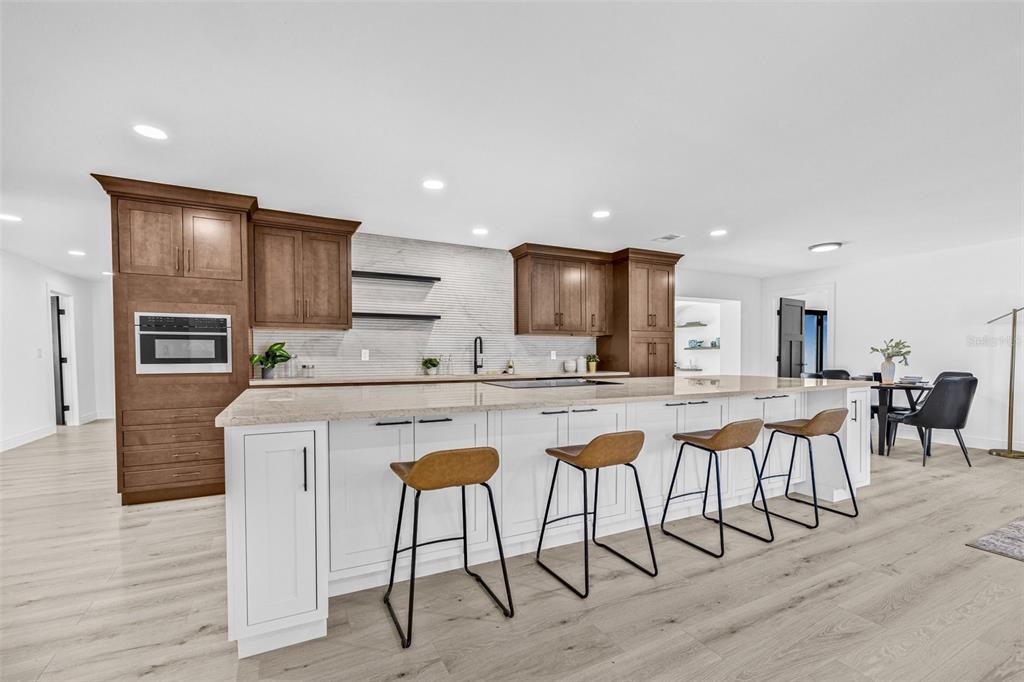 A modern kitchen features a large white island with bar stools and brown wood cabinetry — 4495 CLEARWATER HARBOR DRIVE S, LARGO, FL