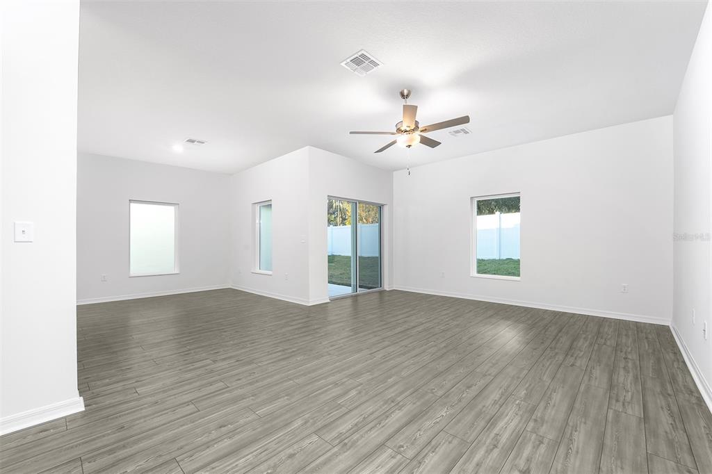 A bright, empty living room features gray wood-look flooring, white walls, and a ceiling fan — 13340 TULA LOOP, ASTATULA, FL