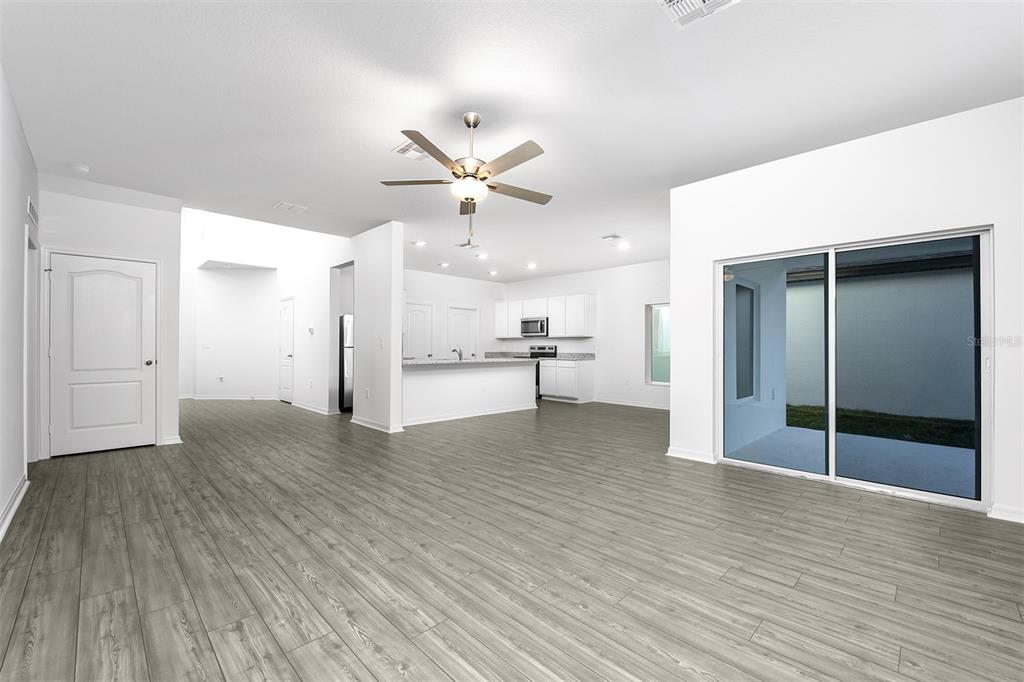 An open-concept living area with gray wood-look flooring, a kitchen island, and sliding glass doors — 13340 TULA LOOP, ASTATULA, FL