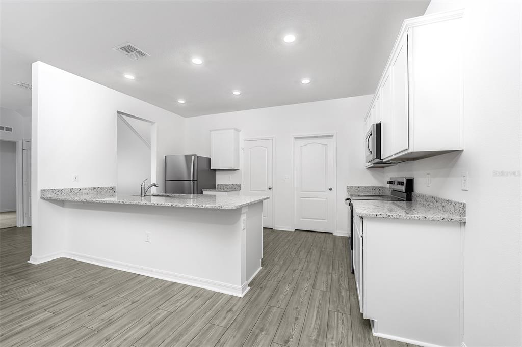A kitchen features white cabinets, granite countertops, stainless steel appliances, and wood-look flooring — 13340 TULA LOOP, ASTATULA, FL