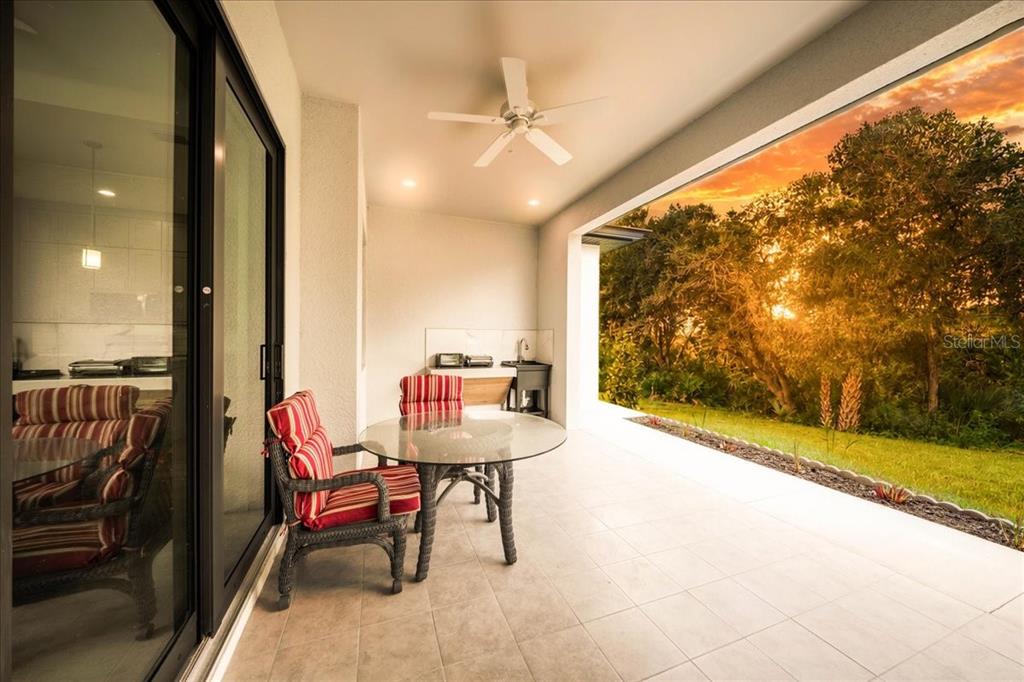 A covered patio features a glass dining table, wicker chairs, and an outdoor kitchen area — 12060 MARGARITA AVENUE, NORTH PORT, FL