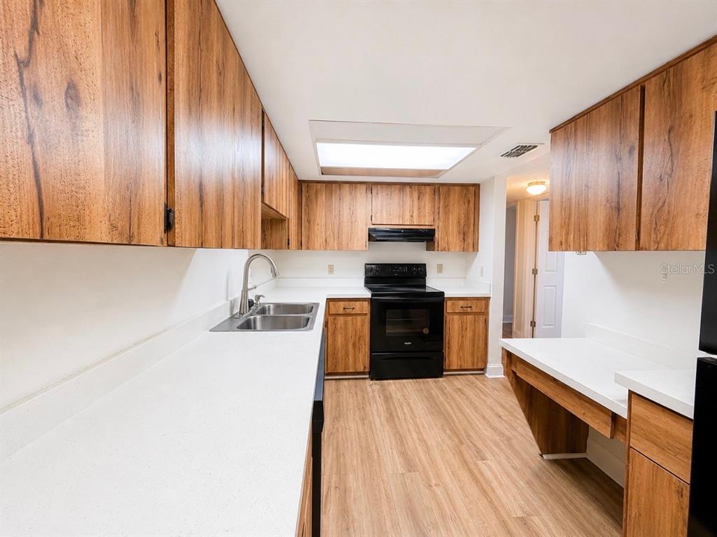 A kitchen with wood-grain cabinets, white countertops, black appliances, and light wood-look flooring — 5541 BAY BOULEVARD UNIT 550, PORT RICHEY, FL
