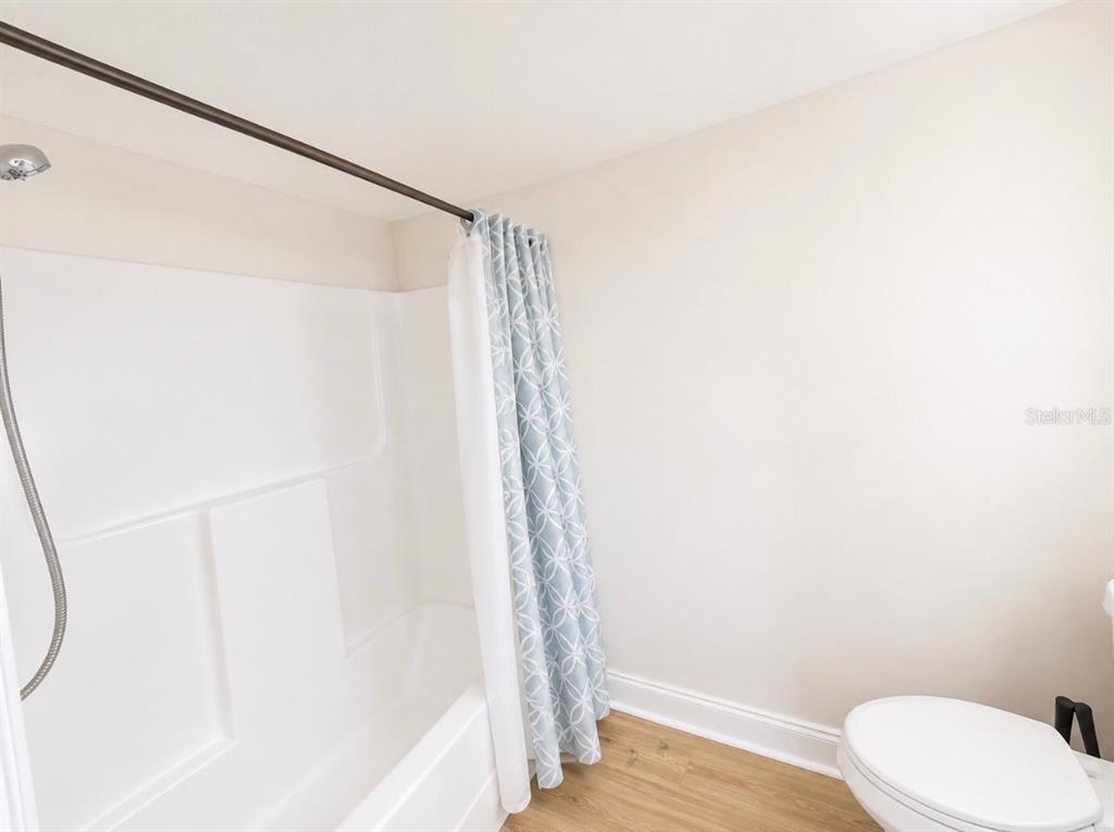 A bathroom features a white tub-shower combo with a patterned curtain and wood-look flooring — 5541 BAY BOULEVARD UNIT 550, PORT RICHEY, FL