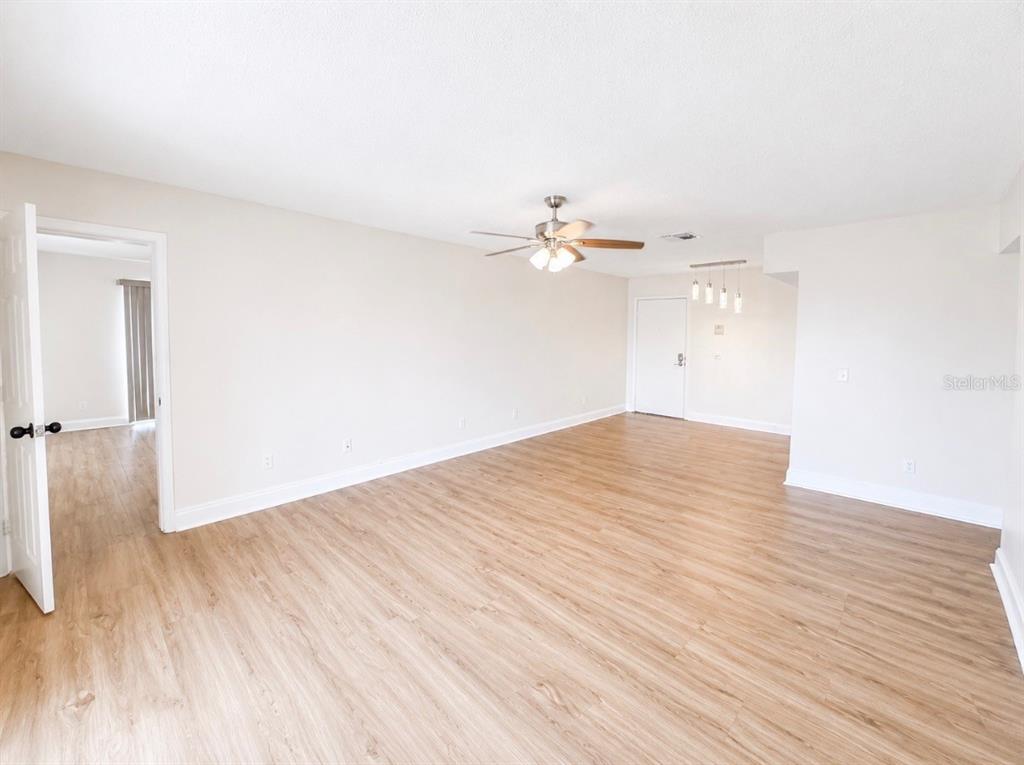 An empty room with light wood-look flooring, white walls, a ceiling fan, and pendant lighting — 5541 BAY BOULEVARD UNIT 550, PORT RICHEY, FL