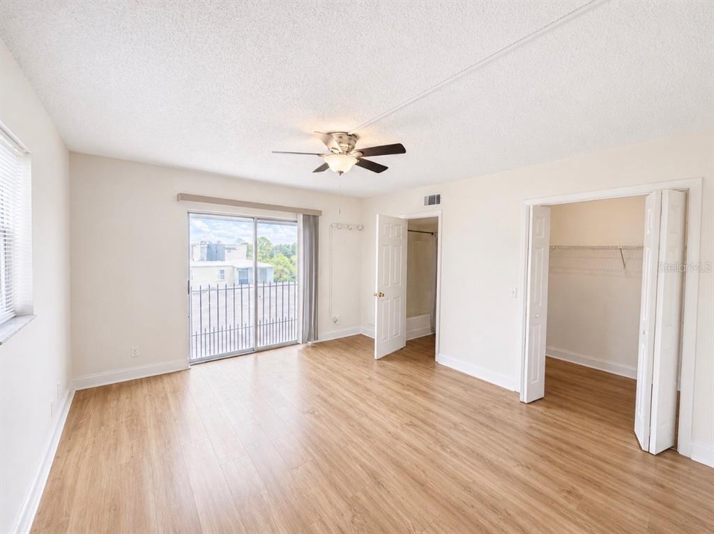 An empty bedroom features light wood-look flooring, a ceiling fan, a sliding glass door, and closet — 5541 BAY BOULEVARD UNIT 550, PORT RICHEY, FL