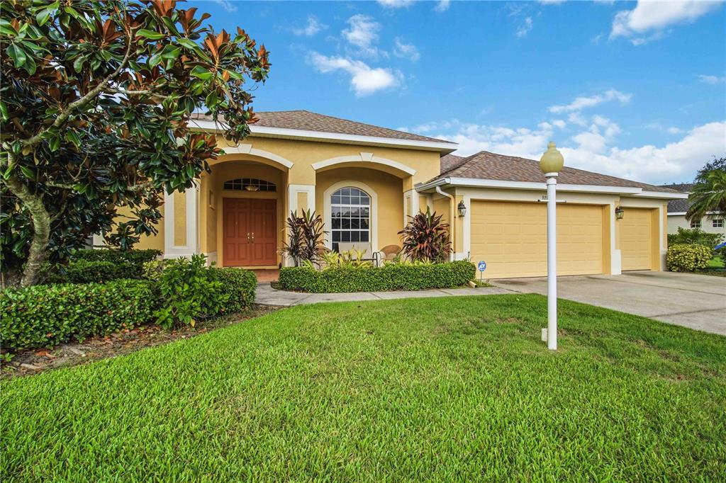 A single-story house with a yellow stucco exterior, a three-car garage, and a front lawn — 9215 63RD COURT E, PARRISH, FL