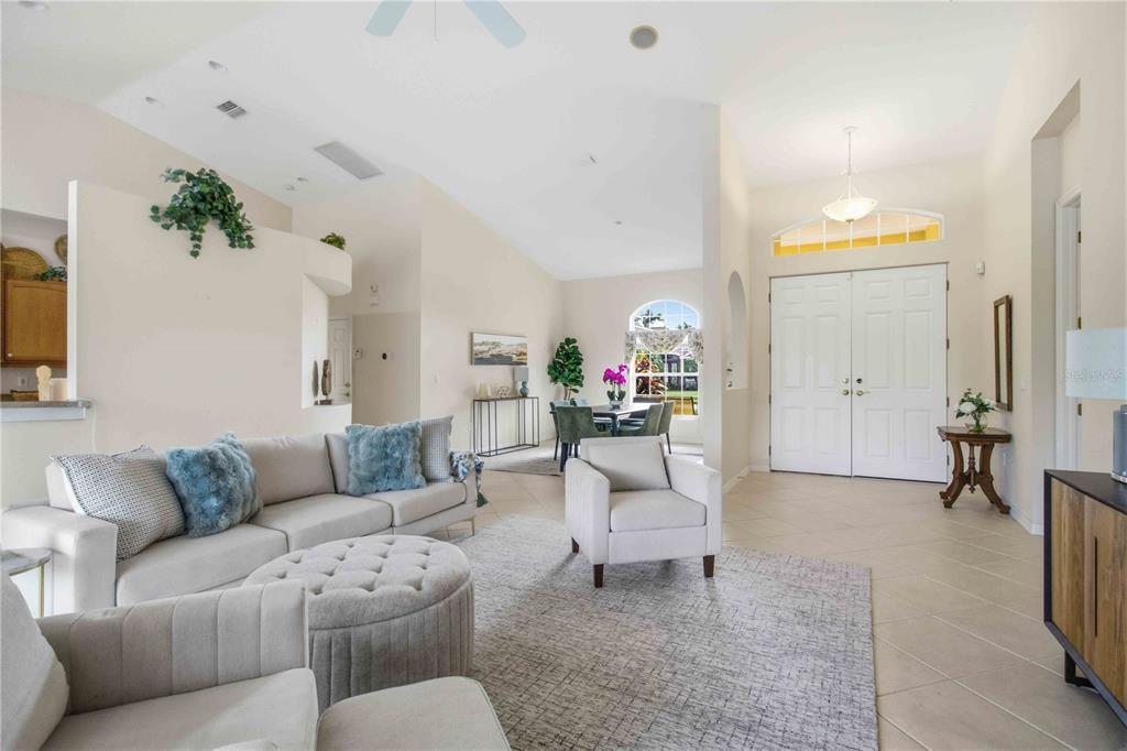 A spacious living room with vaulted ceilings, neutral furniture, and an adjacent dining area — 9215 63RD COURT E, PARRISH, FL