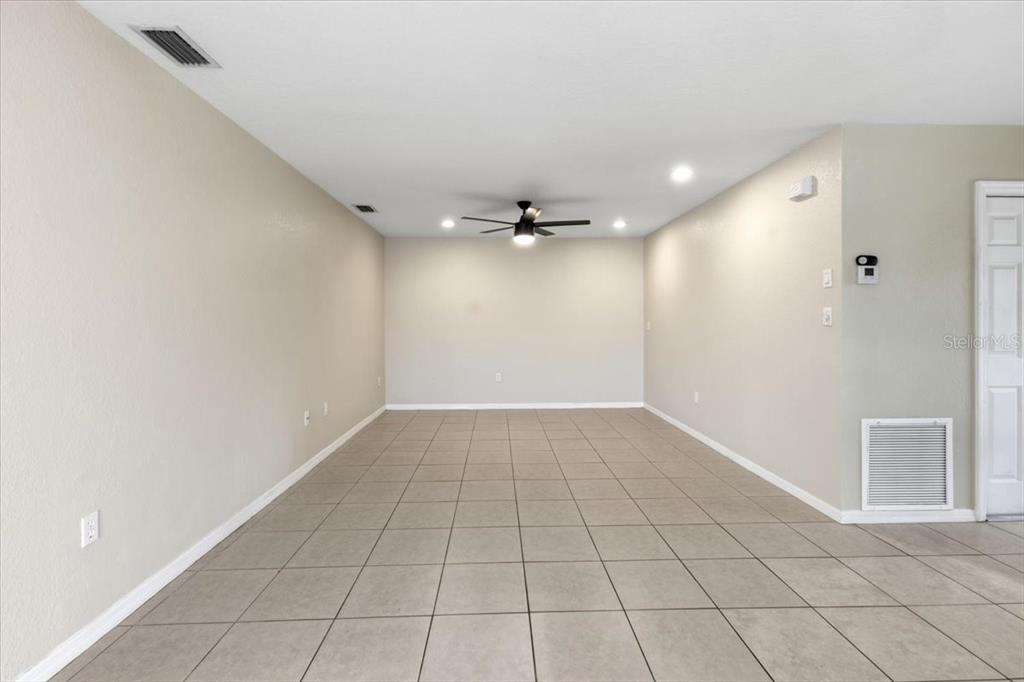 An empty room features light-colored walls, a ceiling fan, and large beige floor tiles — 9216 ANITA AVENUE UNIT A, ENGLEWOOD, FL