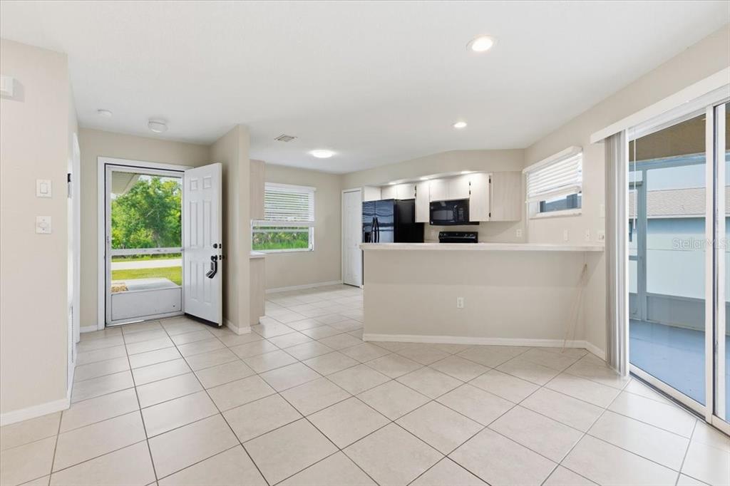 An open-concept kitchen and dining area features light tile flooring, white cabinets, and sliding doors — 9216 ANITA AVENUE UNIT A, ENGLEWOOD, FL