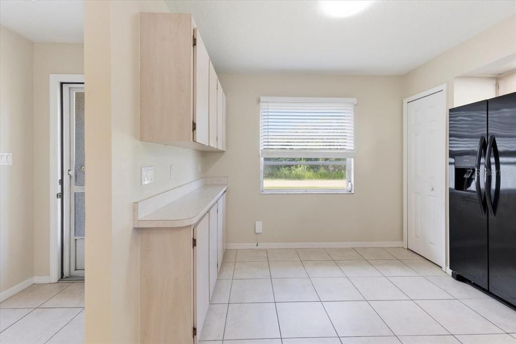 A kitchen with light wood cabinets, white countertops, tile flooring, and a black refrigerator — 9216 ANITA AVENUE UNIT A, ENGLEWOOD, FL