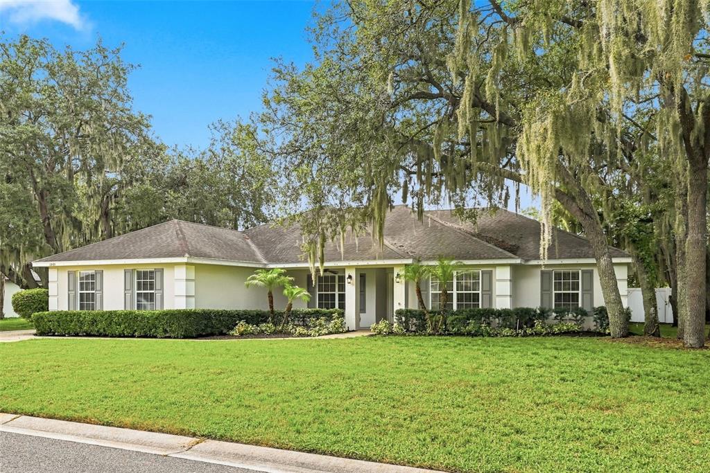 A single-story house with a light-colored exterior, gray shutters, and large oak trees in front — 1845 FARRINGTON DRIVE, LAKELAND, FL