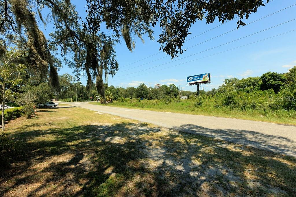 A paved road runs through a grassy area with trees and a distant billboard — 18888 ACKSON STREET, SPRING HILL, FL