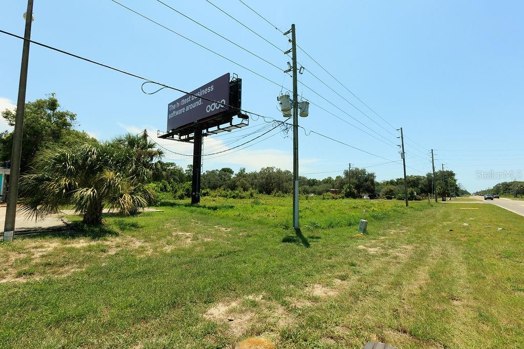 An outdoor view of a vacant grassy lot featuring a large billboard and utility poles — 18888 ACKSON STREET, SPRING HILL, FL