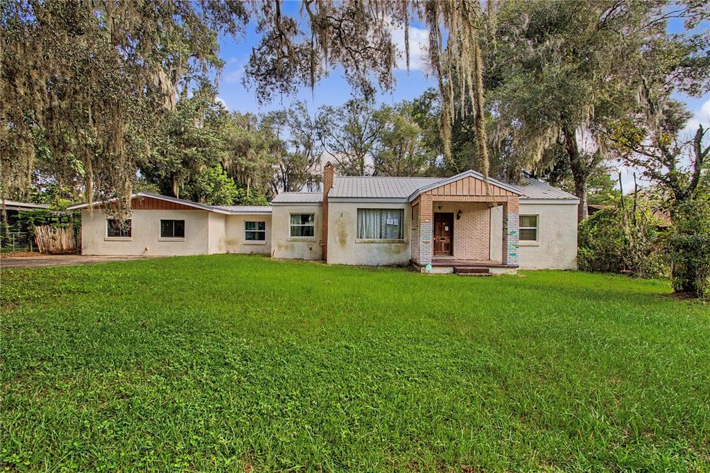 A single-story house with a light-colored stucco exterior and a metal roof sits on grass — 20179 THE GRANADA, DUNNELLON, FL
