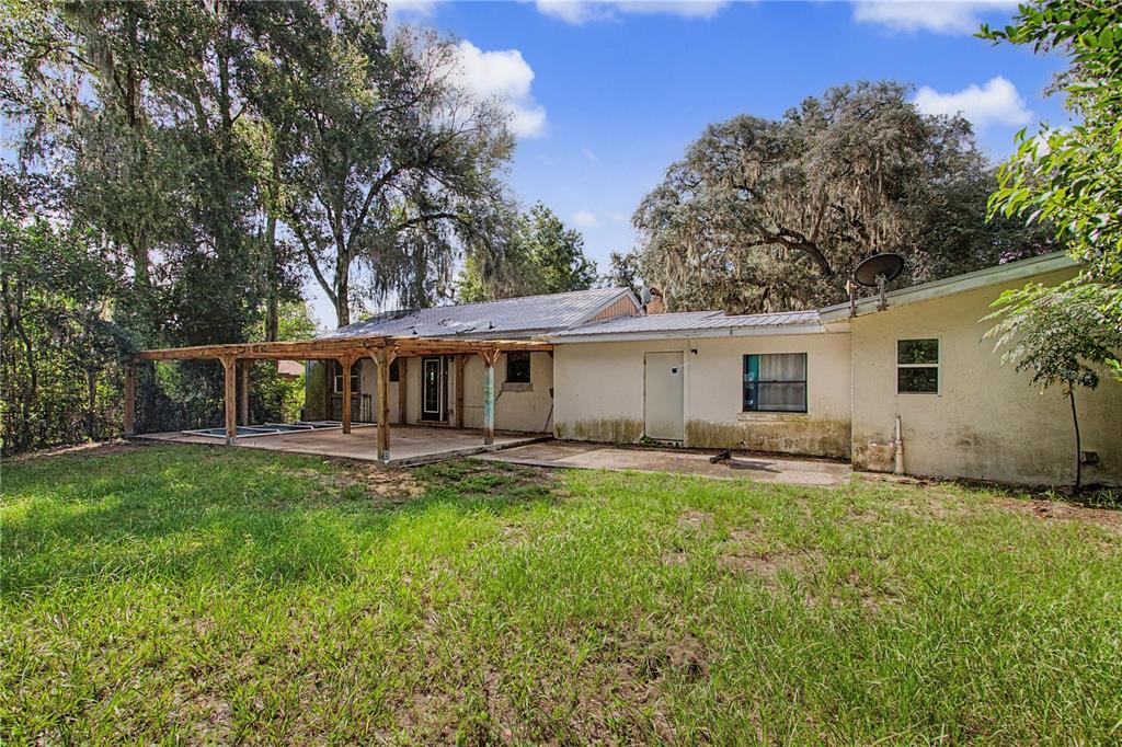 The exterior of a single-story house features a covered patio and a large grassy yard — 20179 THE GRANADA, DUNNELLON, FL