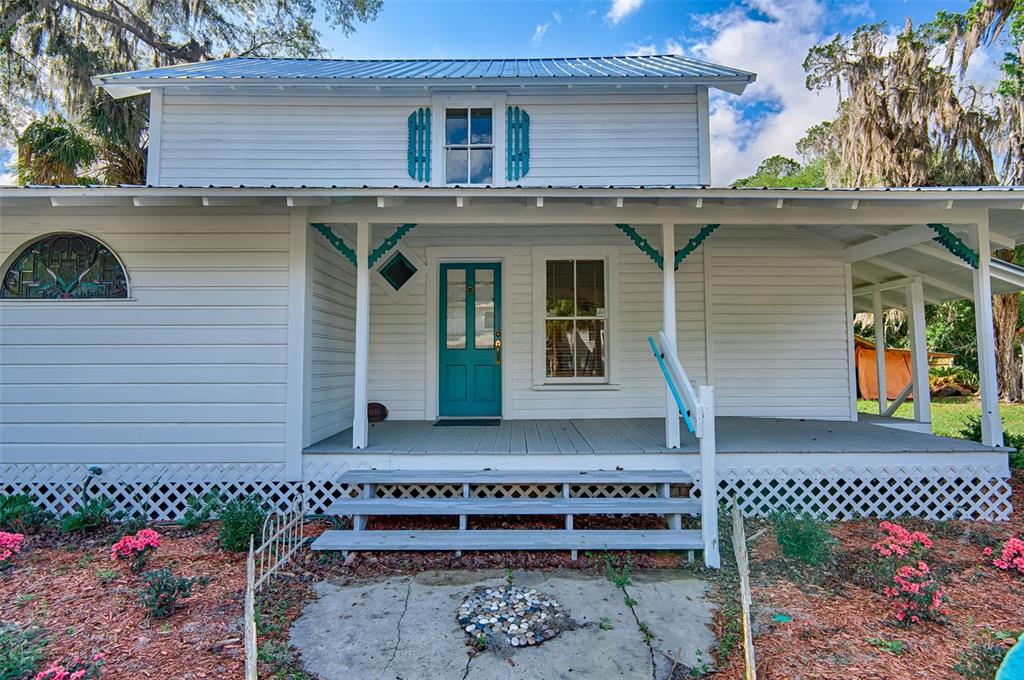 A white house with a teal front door, a front porch, and a metal roof — 25415 NE STATE ROAD 26, MELROSE, FL