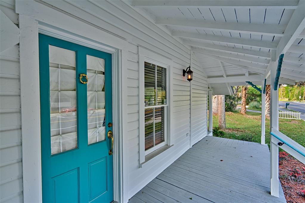 A covered front porch with a teal door and white siding on a house exterior — 25415 NE STATE ROAD 26, MELROSE, FL