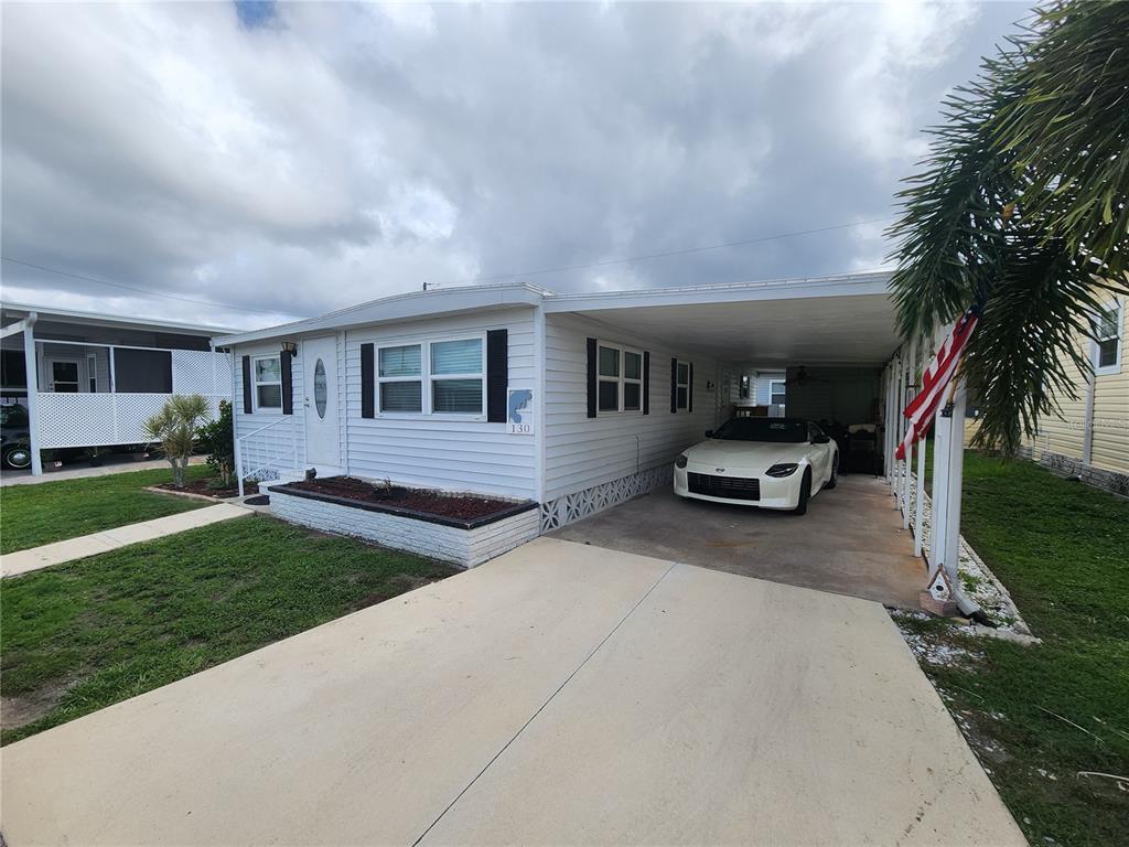 A white mobile home with a carport and a parked car under a cloudy sky — 130 CAPRI DRIVE, PALMETTO, FL