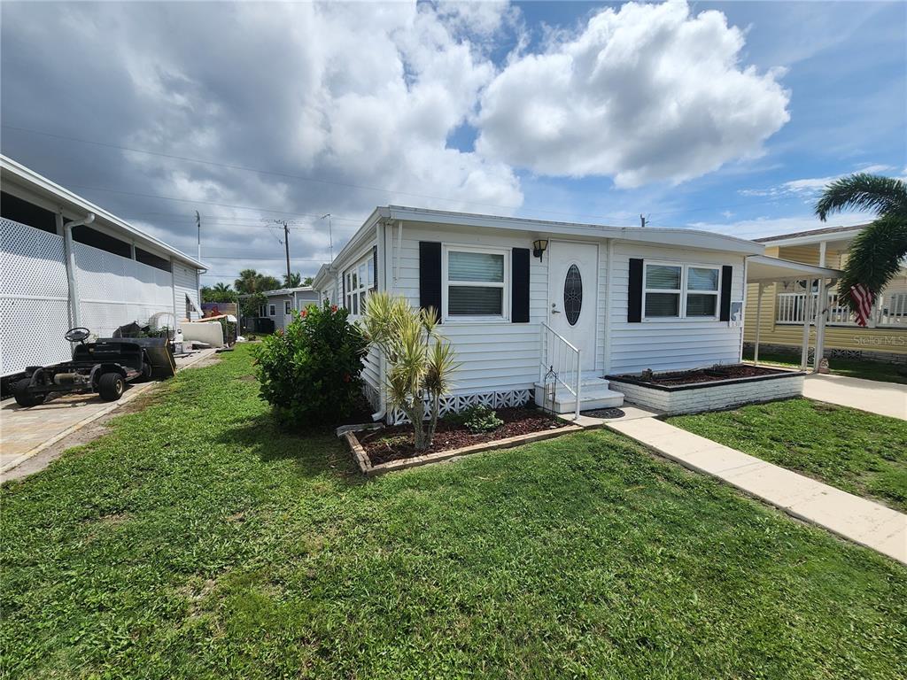 A white mobile home with black shutters and a small front yard under a cloudy sky — 130 CAPRI DRIVE, PALMETTO, FL