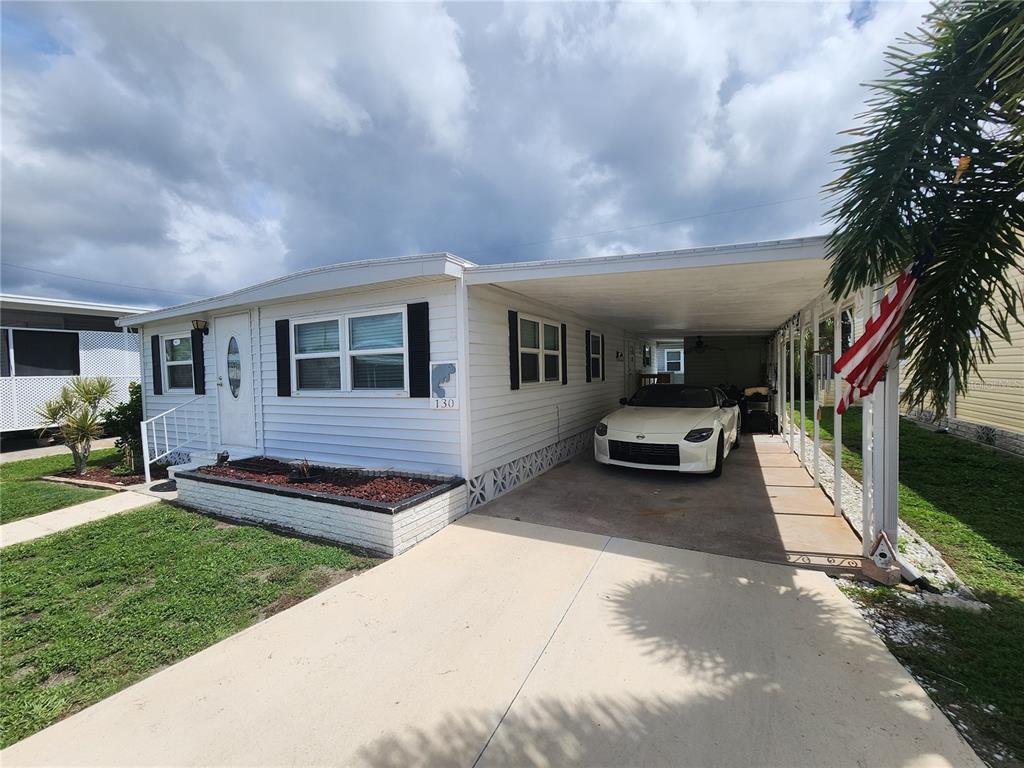 A white mobile home features a carport, a concrete driveway, and a small front garden — 130 CAPRI DRIVE, PALMETTO, FL