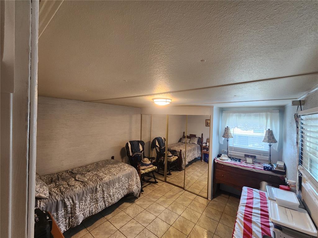 A bedroom with tile flooring, a single bed, mirrored closet doors, and a window — 130 CAPRI DRIVE, PALMETTO, FL