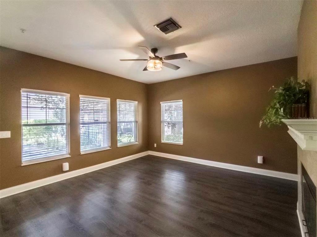 A living room with brown walls, dark wood-look flooring, a ceiling fan, and four windows — 7174 REGINA WAY, ORLANDO, FL