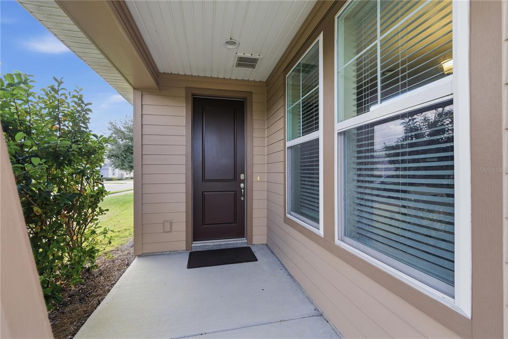A covered front porch features a dark brown door, light tan siding, and large windows — 5504 NW 40TH LOOP, OCALA, FL