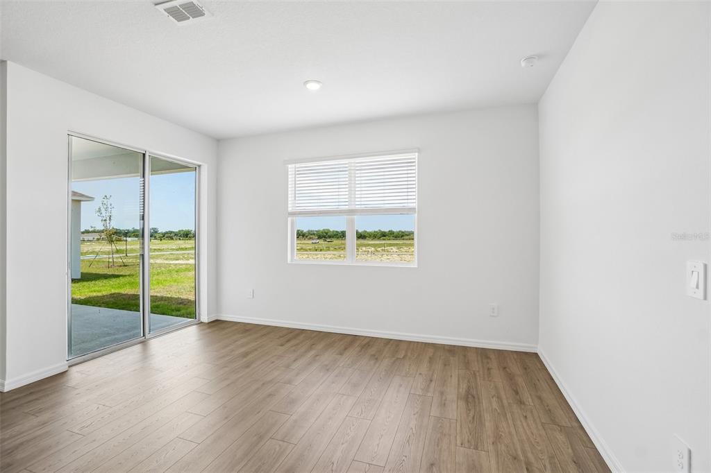 An empty room with light wood-look flooring, white walls, a sliding glass door, and windows — 4660 BARBERRY AVENUE, LAKELAND, FL