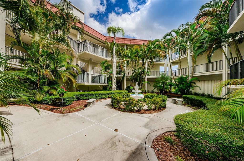An outdoor courtyard with a central fountain, concrete walkways, landscaping, and multi-story apartment balconies — 2700 BAYSHORE BOULEVARD UNIT 2207, DUNEDIN, FL