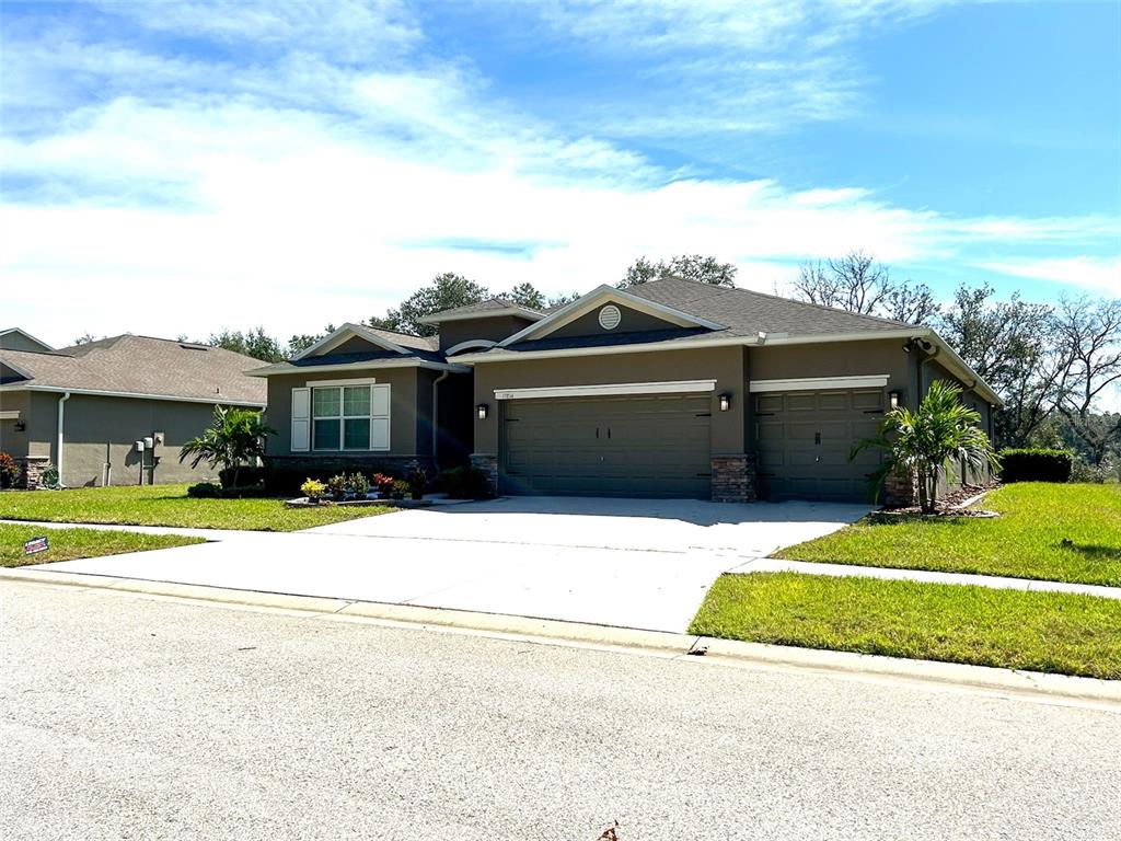 A single-story house with a three-car garage and a concrete driveway under a blue sky — 13814 BEE TREE COURT, HUDSON, FL