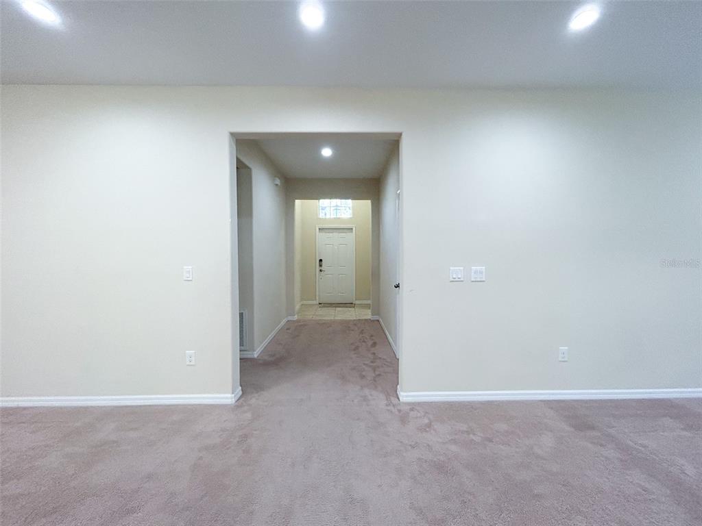 A carpeted room opens into a hallway leading to a white front door — 13814 BEE TREE COURT, HUDSON, FL