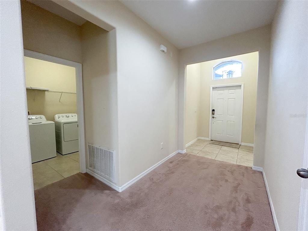 An interior view shows a carpeted entryway leading to a front door and laundry room — 13814 BEE TREE COURT, HUDSON, FL
