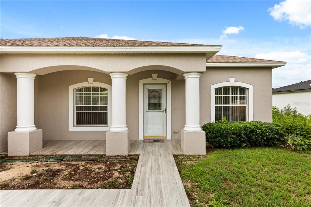 A tan house exterior features a covered porch with three white columns and tiled flooring — 3544 SW 157TH LOOP, OCALA, FL
